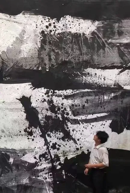 人物站在大型水墨作品旁，观看墨迹与泼墨纹理