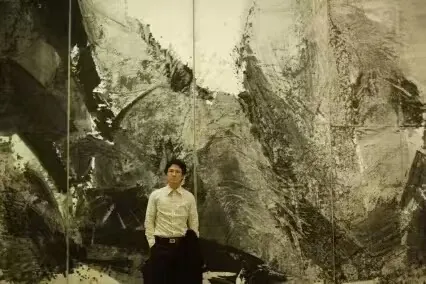 人物站在灰黑色大型水墨画面前